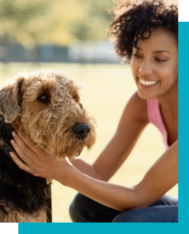 A woman petting her dog 's face while sitting on the ground.